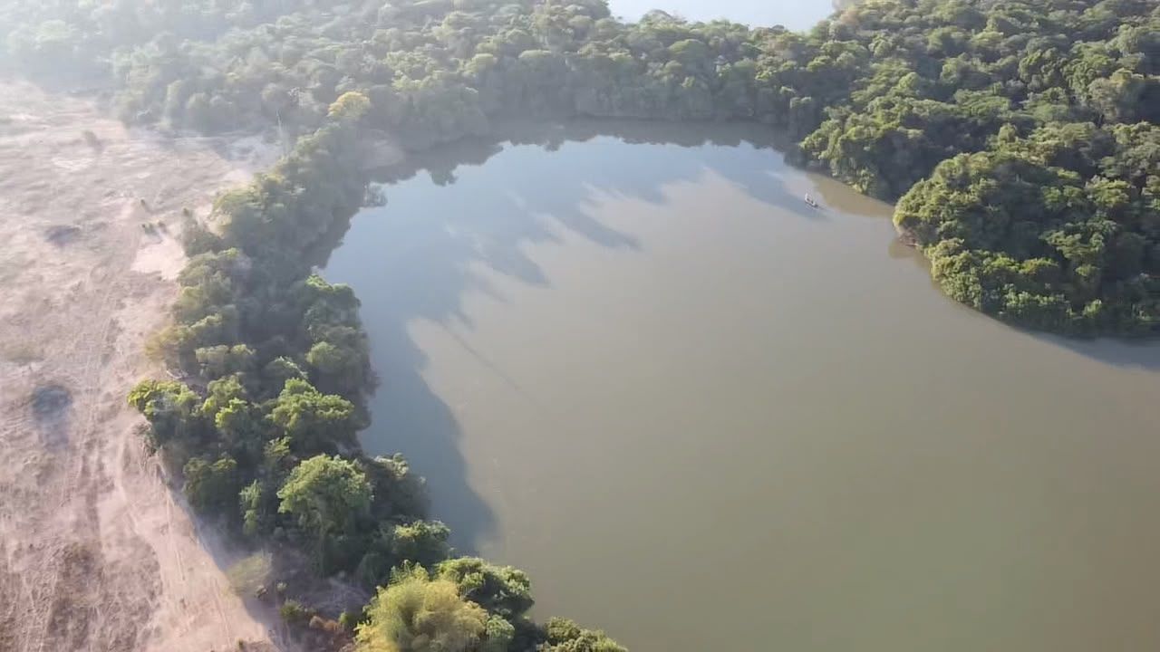 Aerial view of a river lagoon framed by forest, with a fishing boat on the water