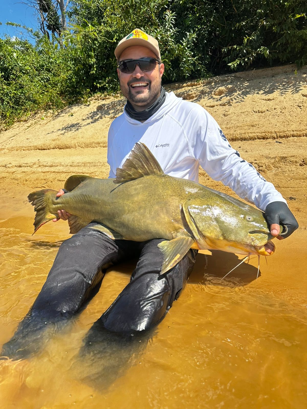 Angler kneeling in shallow water holding a large jaú catfish