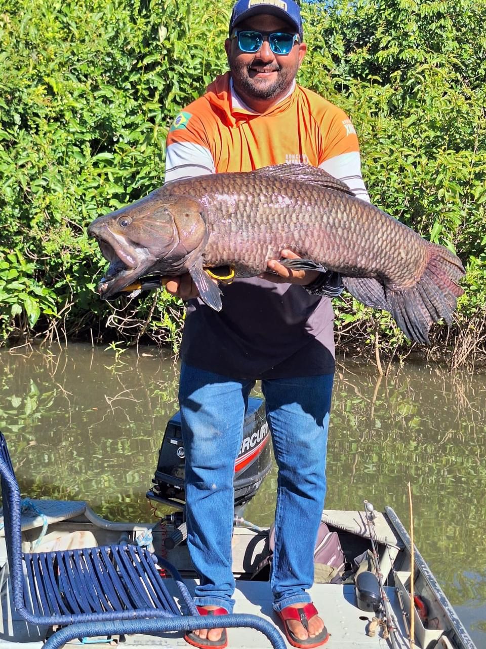 Angler in an orange fishing shirt holding a trairão on the boat